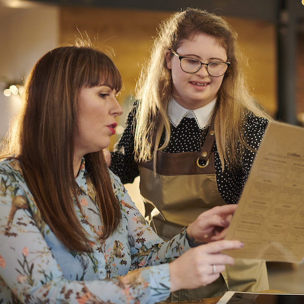 A server and a customer in a restaurant review gluten-free options on a menu